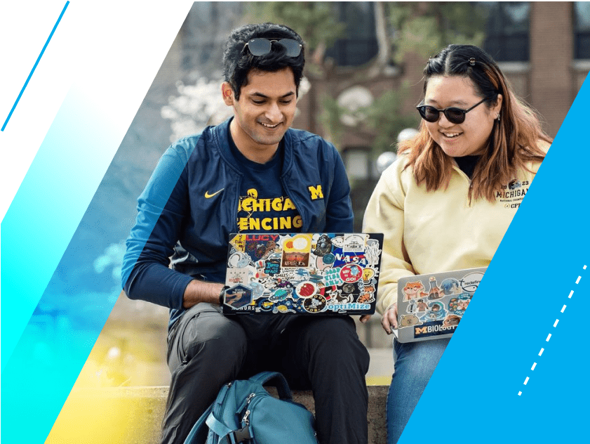 LSA Scholarship students Sanil Mittal and Sharon Gim sit on a cement bench in the Diag. They have sticker-covered laptops open on their laps, and are both smiling and looking at something on Sanil’s laptop screen. 