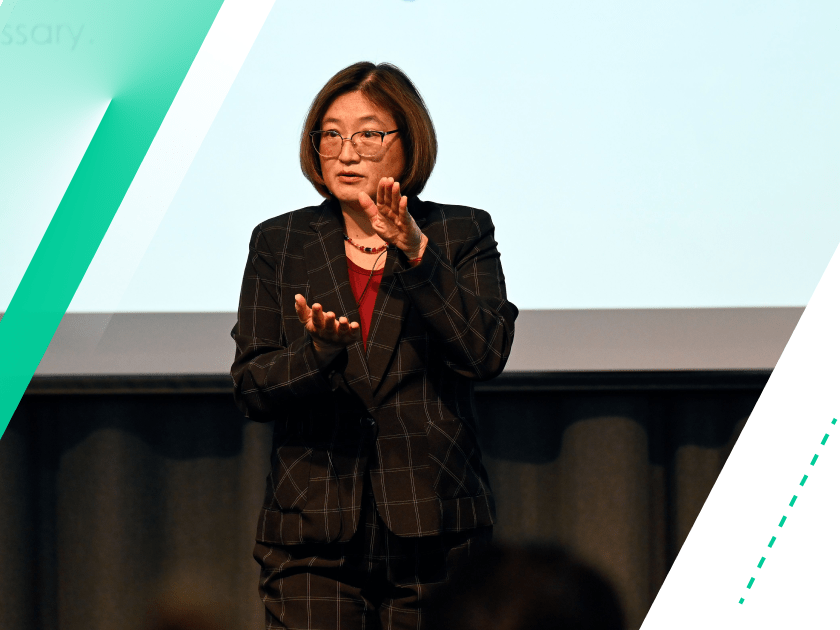 Professor Ann Chih Lin—the Kenneth G. Lieberthal and Richard H. Rogel Professor of Chinese Studies and Associate Professor, Gerald R. Ford School of Public Policy—gives a lecture onstage in front of an illuminated screen. She she is extending her hands in front of her, gesturing in a manner to indicate a distance. 
