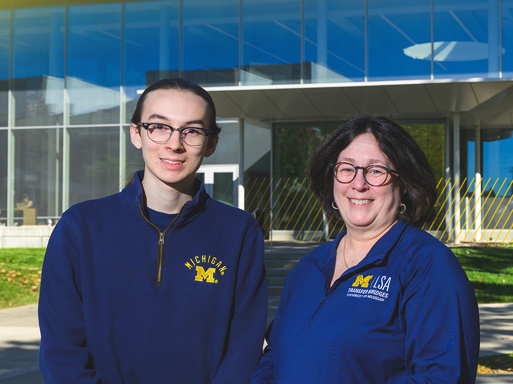 Alan and Linda, a son and mother in blue U-M gear, stand in front of the LSA building at the University of Michigan on a sunny day.