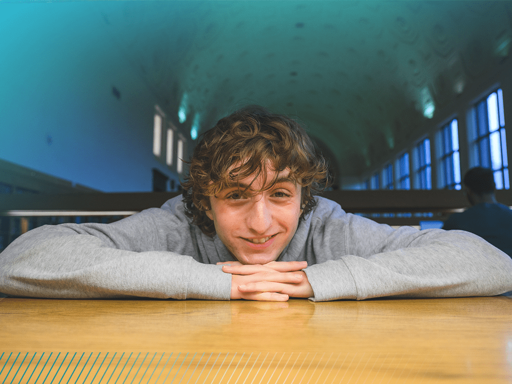 A student looks at the camera with his chin resting on his hands. 