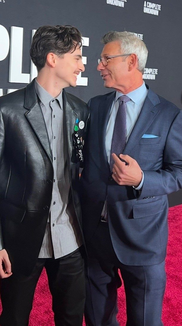 Actor Timothée Chalamet, in a black leather blazer, embraces LSA alum Peter Jaysen, who wears a blue suit.