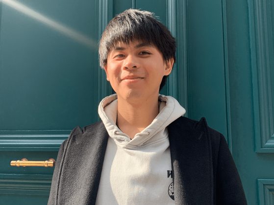 A photograph of Shao-Chi Ou smiling at the camera. He is wearing a gray hoody and black coat.