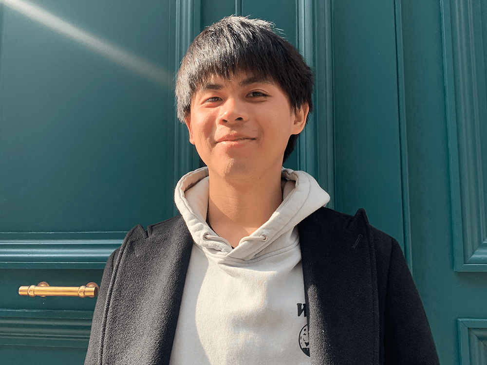 A photograph of Shao-Chi Ou smiling at the camera. He is wearing a gray hoody and black coat.