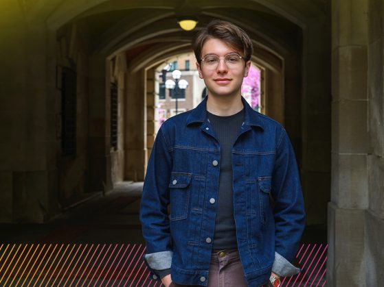 A person wearing glasses stands in front of an archway.