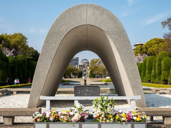A photo of the Cenotaph for the Victims of the Atomic Bomb sculpture in Hiroshima, Japan, with flowers in the foreground.