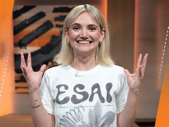 A woman wearing a white T-shirt that says "ESAI" smiles and holds her hands in the air.