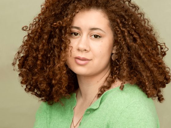 A photograph of a curly-haired woman wearing a green sweater.