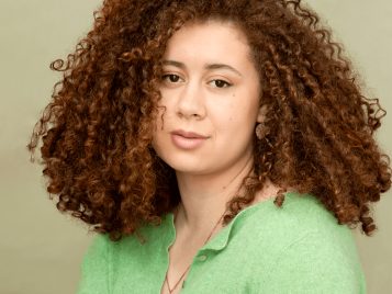 A photograph of a curly-haired woman wearing a green sweater.
