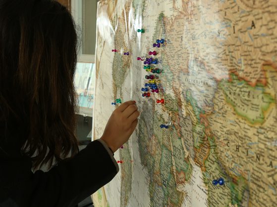 A student stands before a map of the world hanging from a bulletin board. She inserts a pushpin in the northern part of Africa.