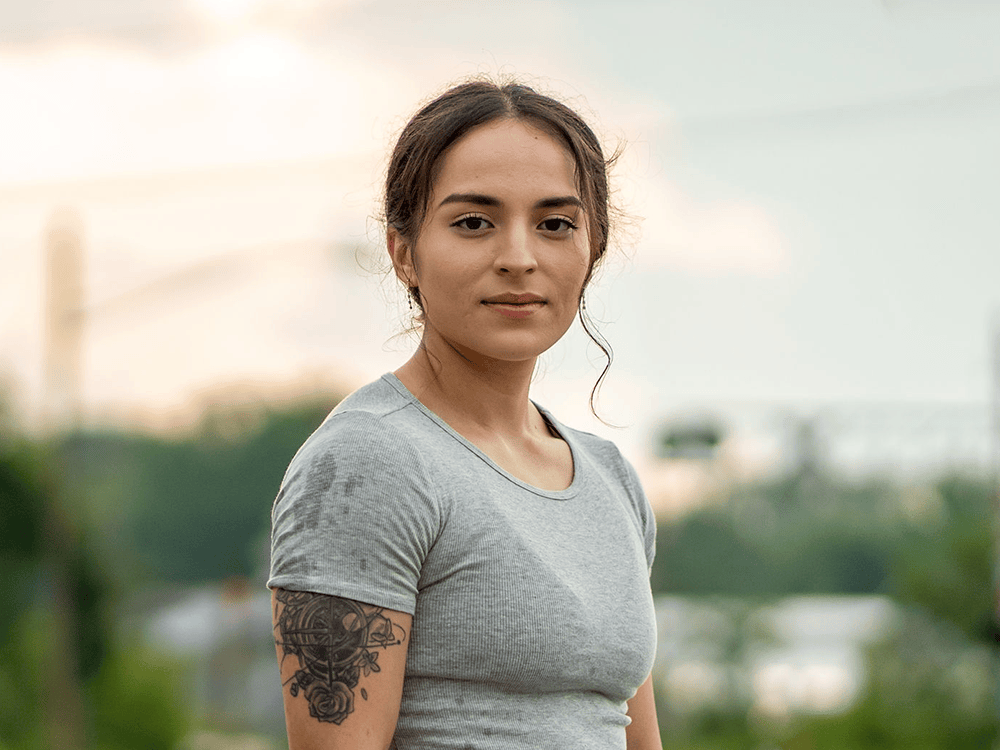 Isabel Stasa faces the camera in a three-quarter profile with a neutral expression, with a park out of focus in the background.