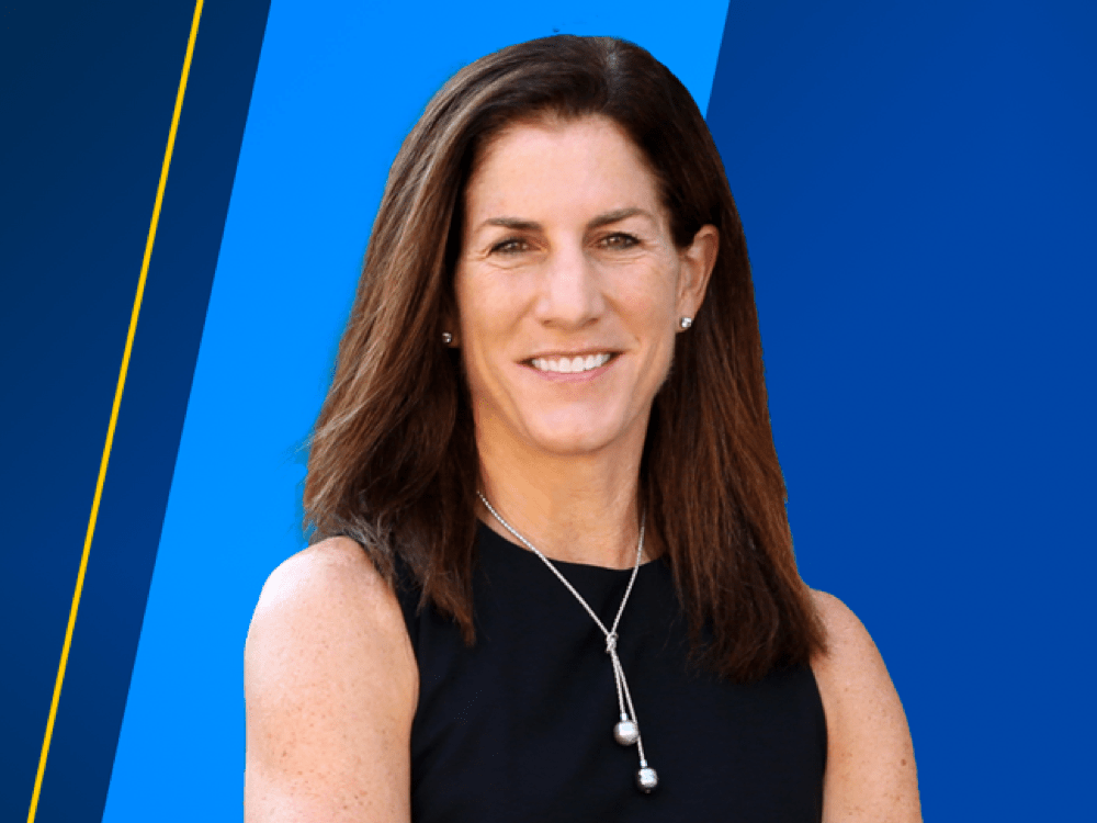 Dean Anne Curzan stands with arms crossed in front of a blue banner.