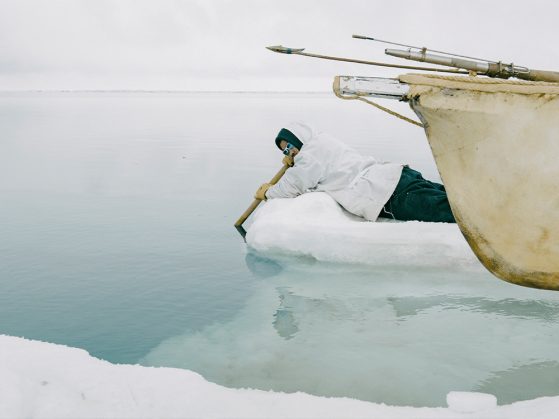 An Indigenous man listens for whales through an oar