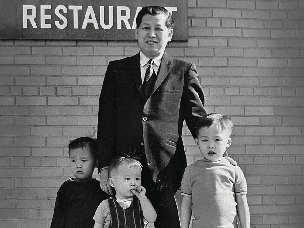 A photo of a man in a suit and three small children standing in front of a restaurant sign.