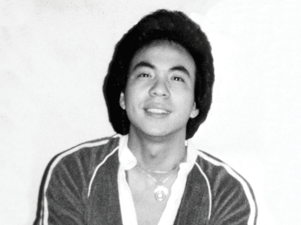 A black and white photo of Vincent Chin, a young man wearing a v-neck shirt and smiling. He is wearing several necklaces. 