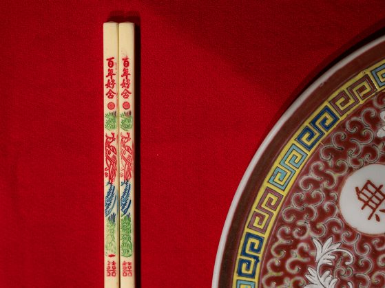 A close-up photo of a pair of chopsticks and an ornate plate laid upon a red napkin. 