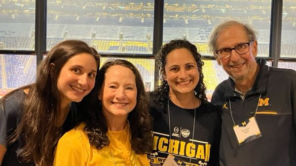 The four members of the Woll family smile in a suite at Michigan Stadium. The window in the background overlooks the action on the football field.