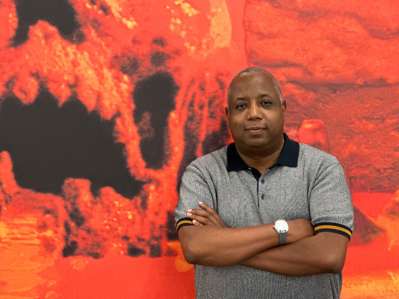 Kemp Powers standing with his arms crossed in front of a red background