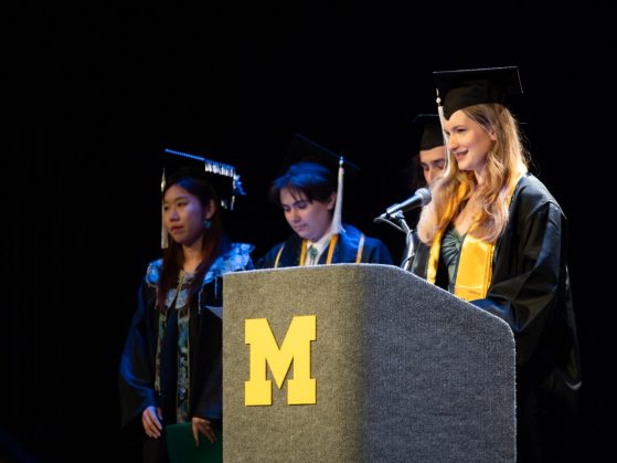 Students at a podium in graduation caps. 