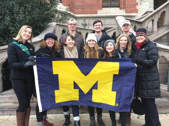 group of U-M students on the steps of a building in Helsingborg, Sweden, holding a U-M maize and blue flag