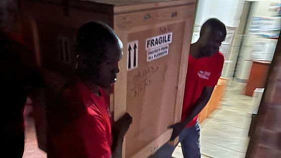 Two people carry a large crate that says fragile.