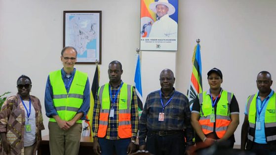 Six people standing in a row. Some are wearing green and orange vests and nametags.