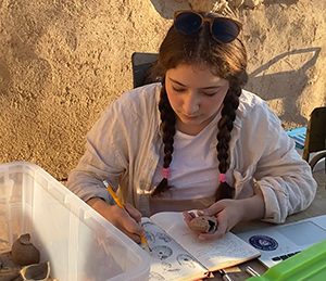 IPAMAA student Elena Echavarria Gil sitting with pottery fragments and recording pottery markings in her journal.