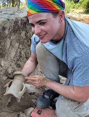 IPAMAA student Julian Skye McCoy in a dig trench holding a piece of ancient pottery