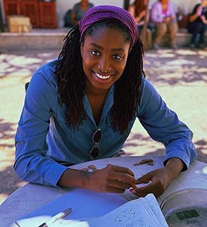 IPAMAA students Felicity Sorenson seated outdoors at a table with artifacts and a journal