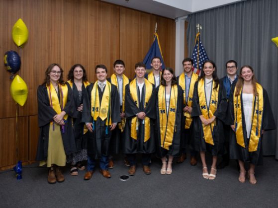 11 students in U-M graduation robes smile in a group picture