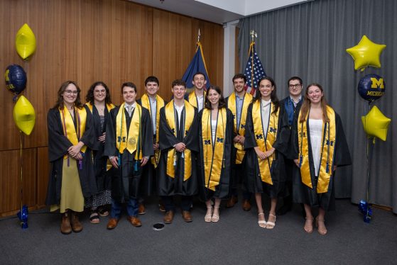 11 students in U-M graduation robes smile in a group picture