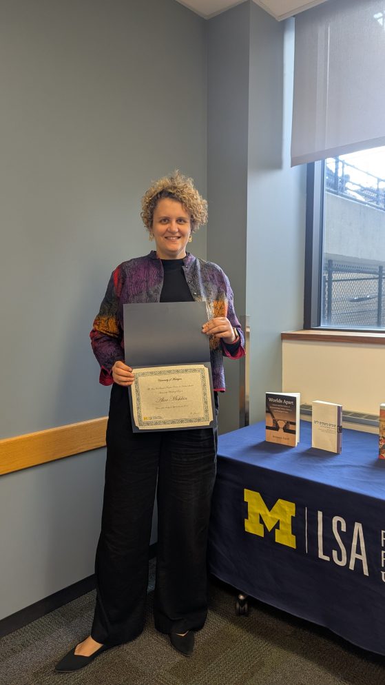 A woman poses holding a certificate awarded to her for academic excellence. 