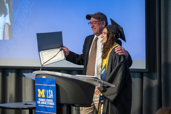 A professor puts his arm around his student's shoulders and faces the audience to present her with an award.