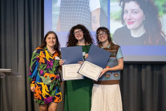 A professor presents an award to two students behind a podium