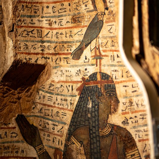 Close-up of a scene from the coffin of the Egyptian priest Djehutymose, a wooden artifact painted with the goddess Amentet in profile. She raises her arms and a falcon is perched on her head, while in the background, rows of hieroglyphs depict the Book of the Dead.
