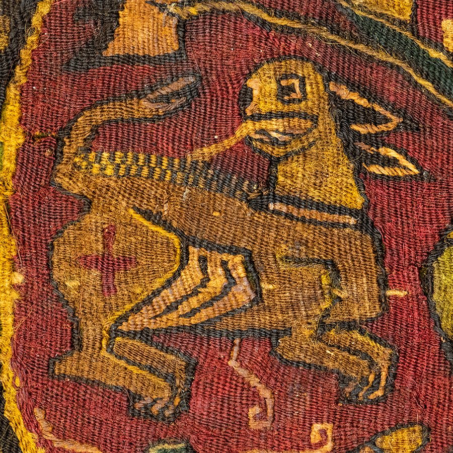 Close-up of a Kelsey Museum textile depicting a highly stylized yellow lion design on a red background.