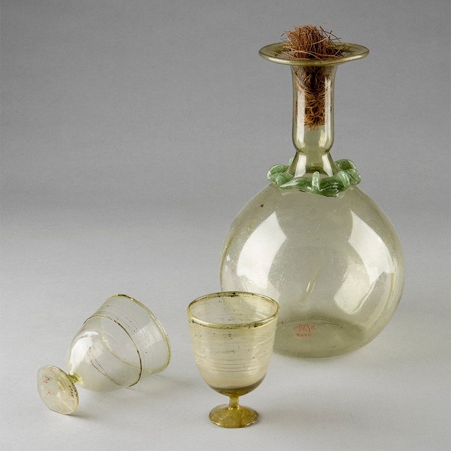 Three green glass vessels—two small cups with stems and a large-bellied flask with a stopper.