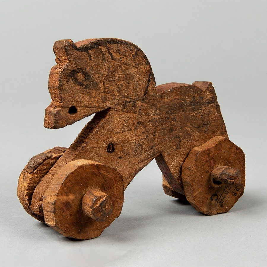 Flat wooden toy carved in the shape of a horse with four wheels attached to its base.