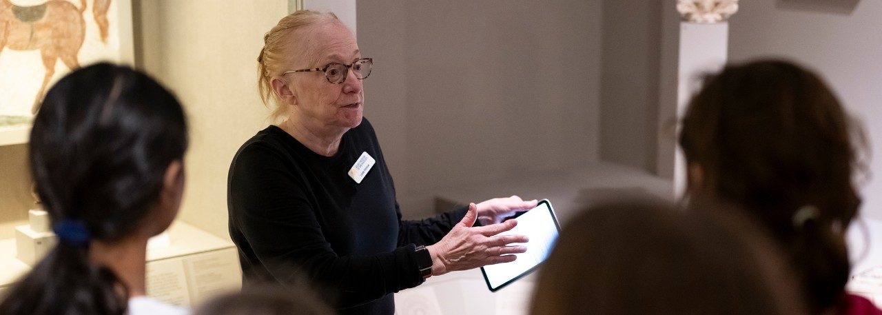 Docent Linda Kimmel holds an iPad while addressing a group of K–12 visitors in the Kelsey Museum’s Roman galleries.