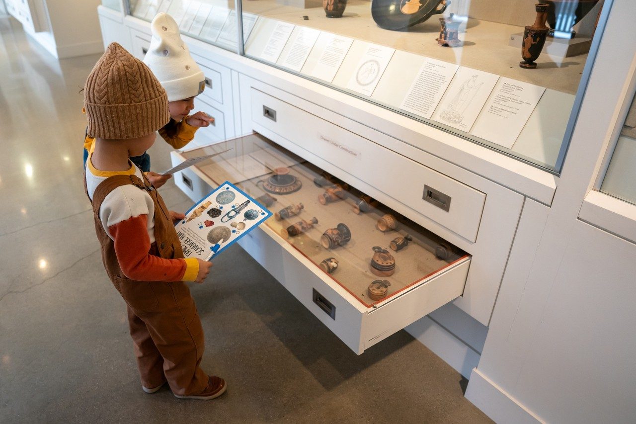 Two children look in a drawer containing artifacts to work on a scavenger hunt.
