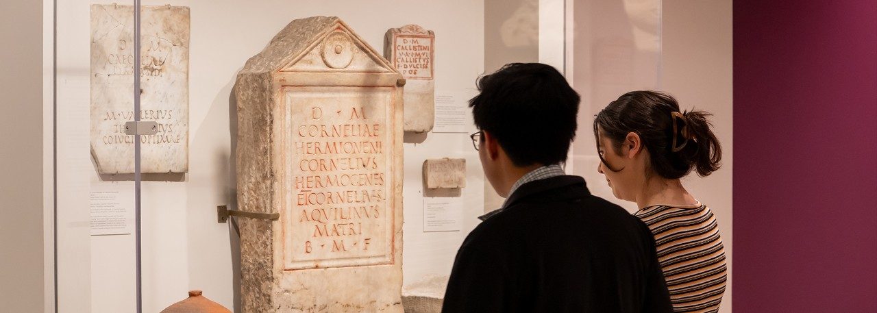 Two visitors look at a group of marble funerary inscriptions on display in the Kelsey Museum.