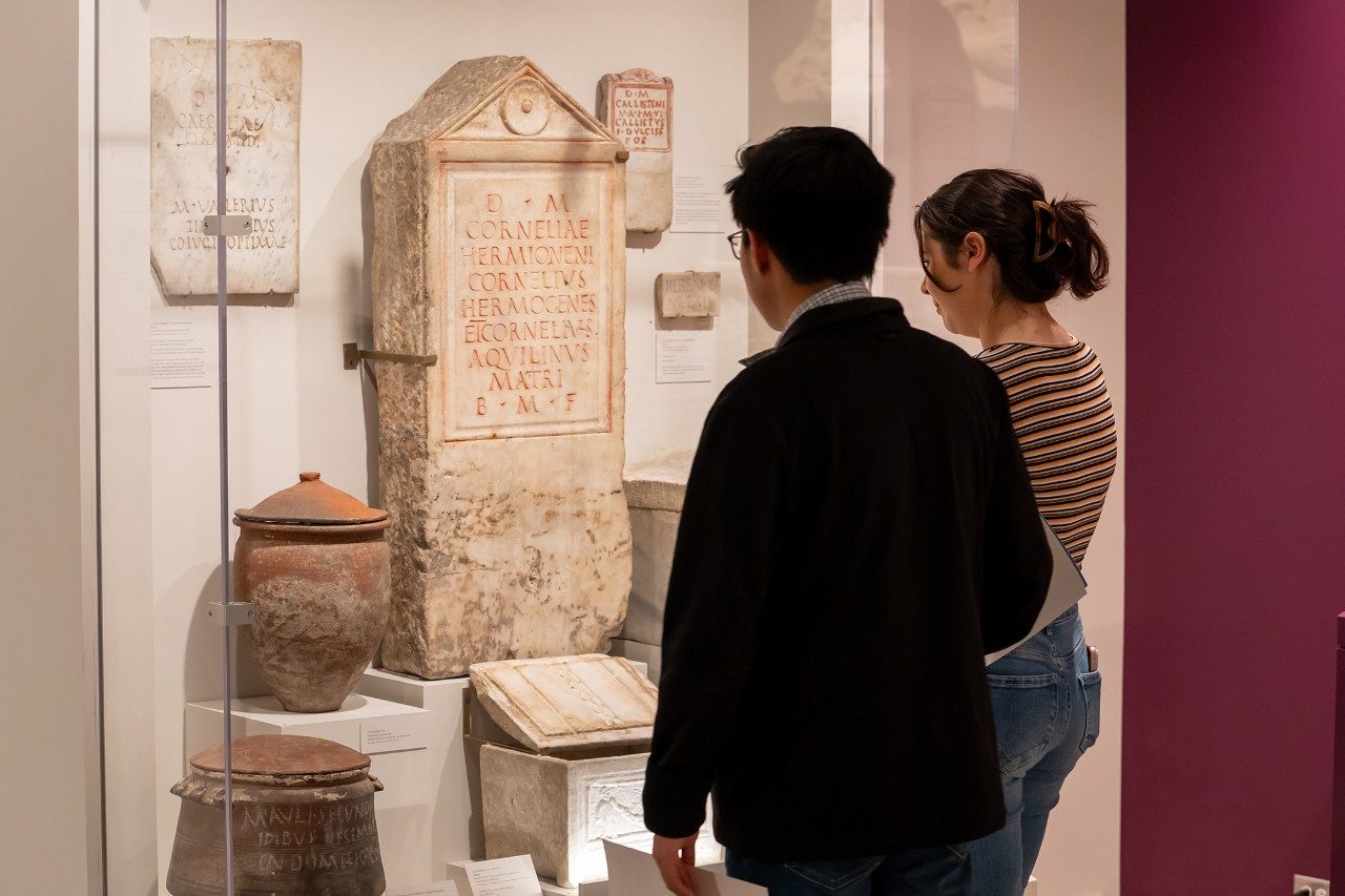 Two adults look at marble inscriptions and other Roman artifacts at the Kelsey Museum.