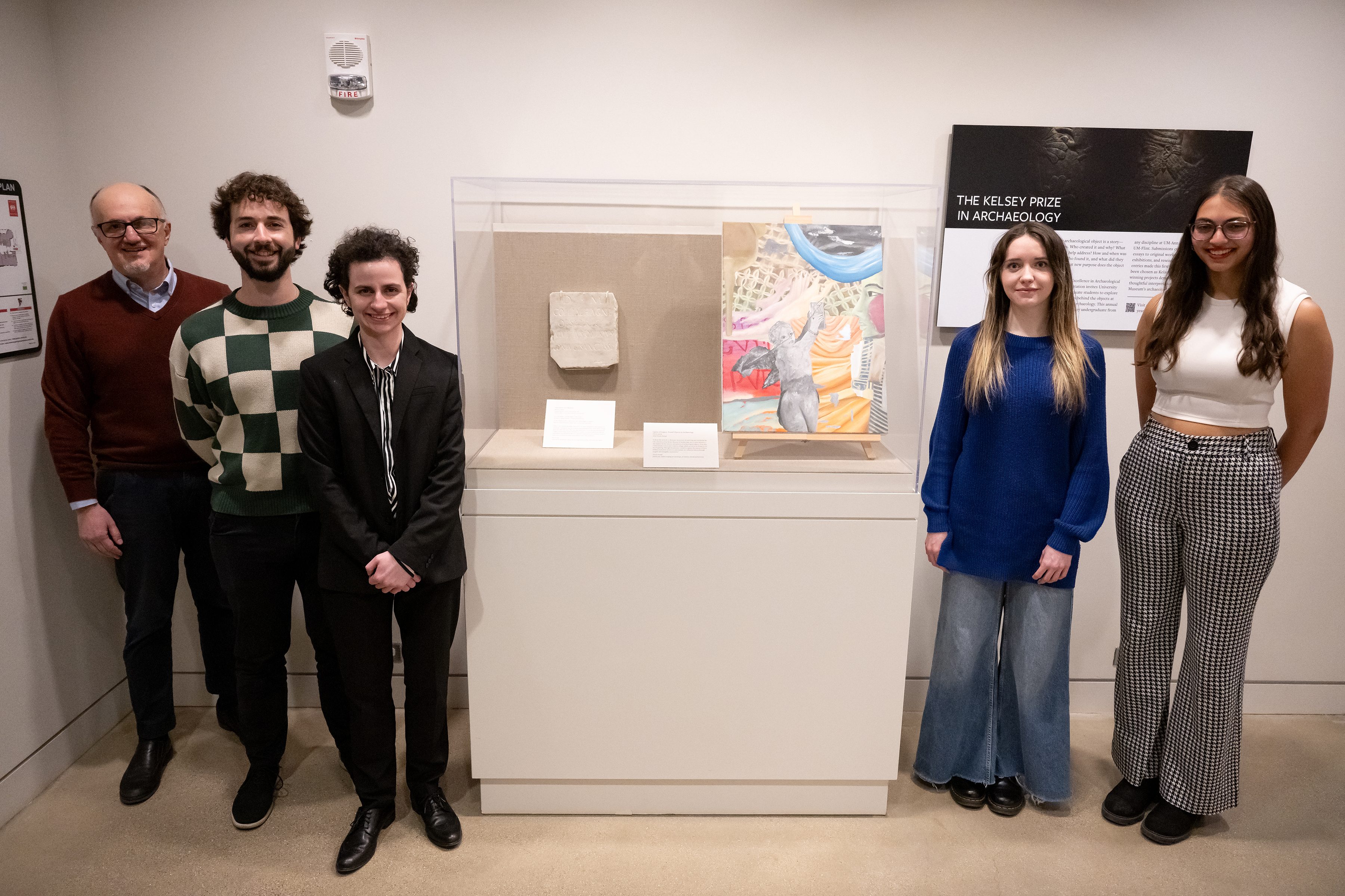 Five people stand on either side of a museum case displaying an inscription and an oil painting.