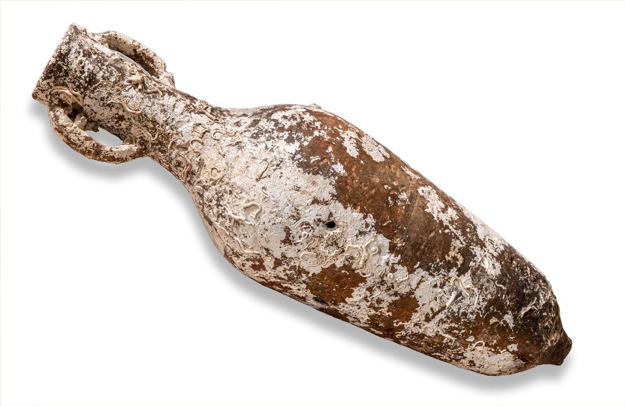 Two-handled, oblong transport amphora with a pointed end. It’s surface is covered in white residue from barnacles.