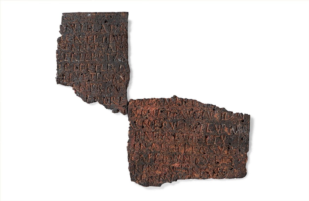 A flat bronze document broken in two pieces containing a long Latin inscription.