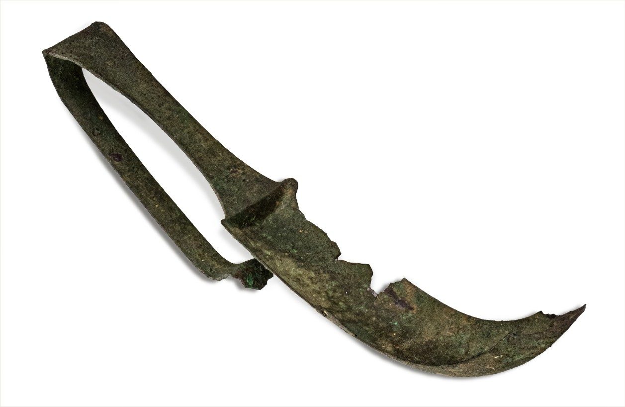 Corroded bronze strigil—a tool with a handle and a curved blade.