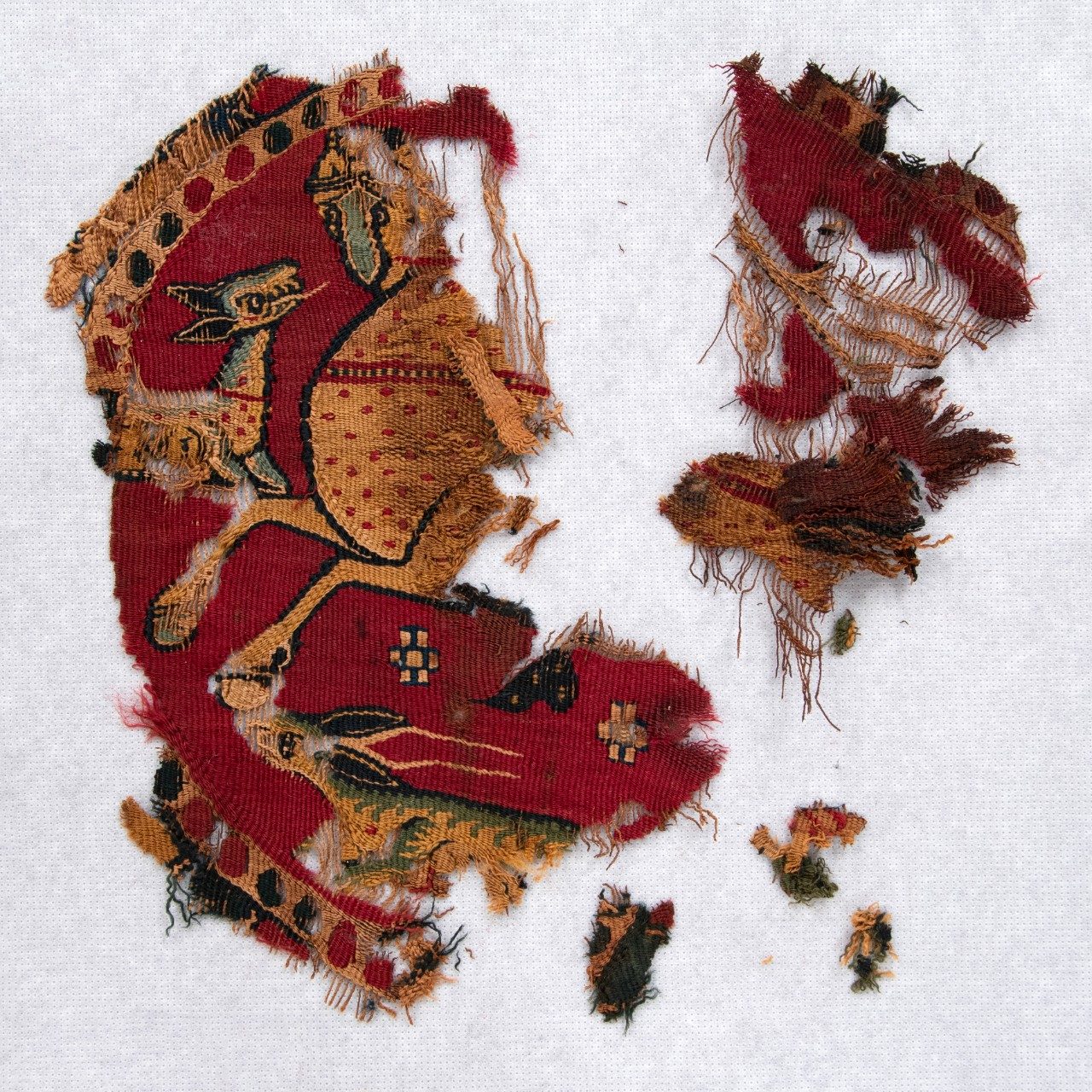 Multiple fragments of a roundel woven from bright-red cloth. A border of dots encircles the stylized image of a yellow, red-dotted horse and two deer similarly colored.