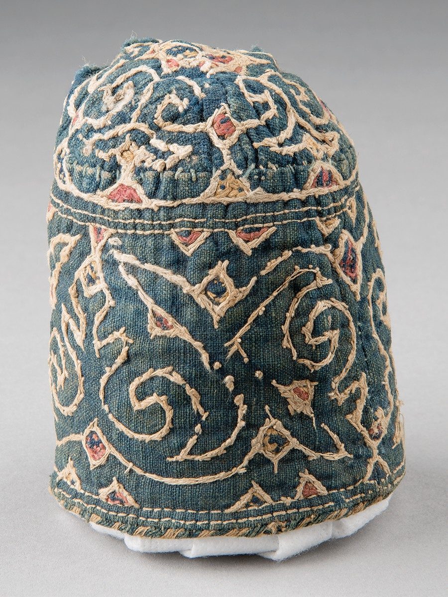 A dark blue conical cap covered in swirling embroidery designs of white, red, and yellow.