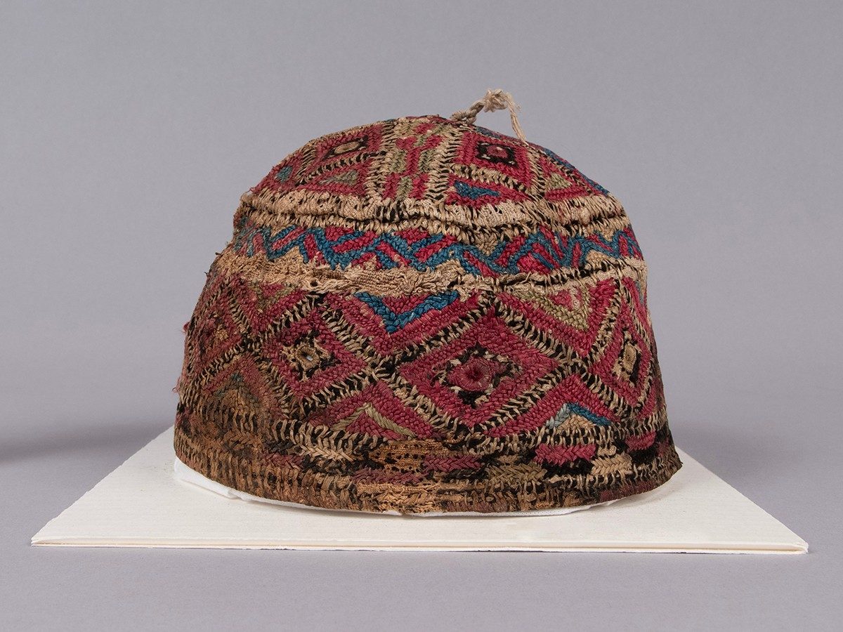 A conical cap covered in geometric woven designs of tan, red, and blue.