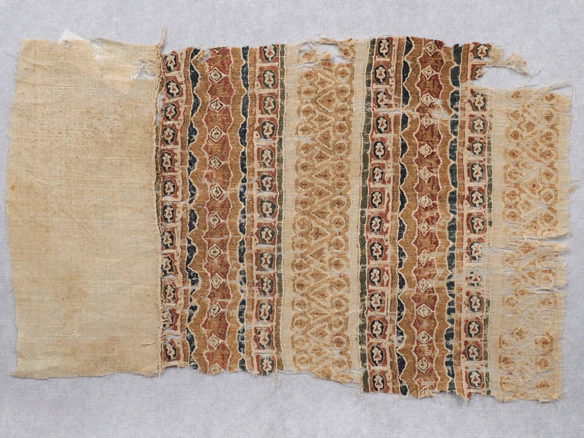 Tan woven textile with brightly red, blue, orange, green, and yellow patterns in repeating bands.