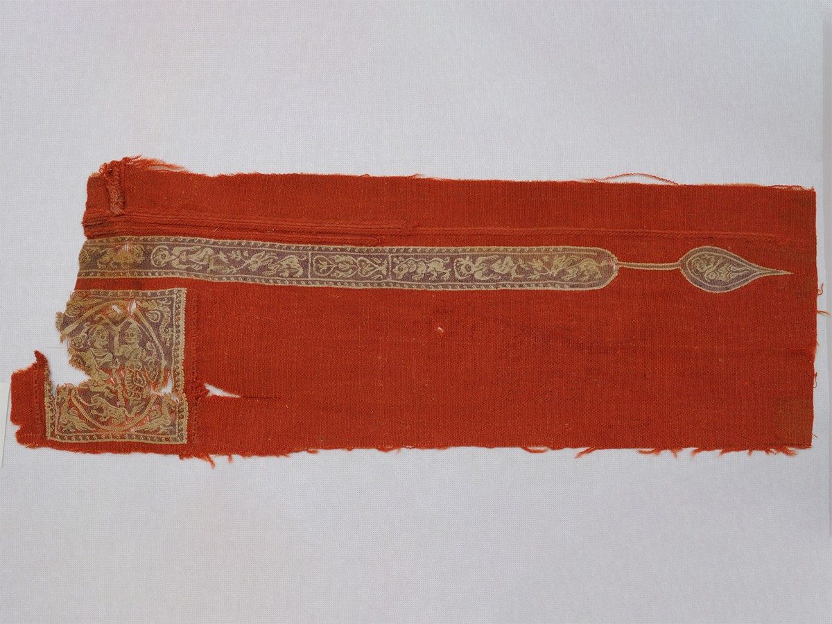 Bright red woven textile with a thin band of tan near the top and a tan square near the bottom left decorated with images of animals.